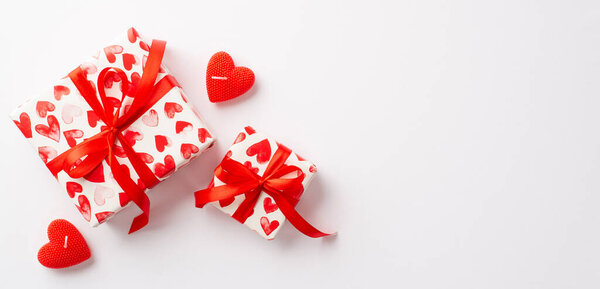 Saint Valentine's Day concept. Top view photo of stylish gift boxes with red ribbon bows and heart shaped candles on isolated white background with empty space