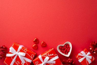 Sevgililer Günü konsepti. Beyaz kurdeleli mevcut kutuların üst görünüm fotoğrafı boş arkaplan ile izole edilmiş kırmızı arkaplanda şekerli kalp şeklinde fincan tabağı