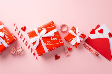 Sevgililer Günü konsepti. Beyaz kurdeleli kırmızı hediye kutularının en üstteki fotoğrafı kalplerle süslü zarf dekoratif bant ve izole edilmiş pastel pembe arka plan klipleri.
