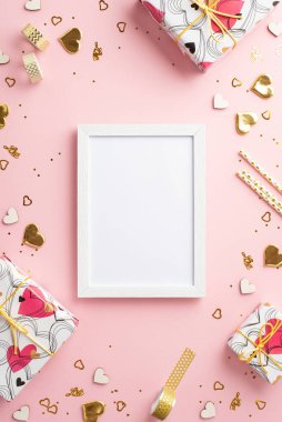Sevgililer Günü konsepti. Fotoğraf çerçevesi son moda hediye kutularının dikey üst görünümü dekoratif bant altın kalpler pulları ve kopyalanmış açık pembe arkaplan üzerindeki konfetileri samanlaştırdı