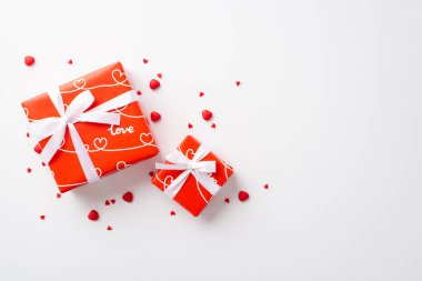 Sevgililer Günü konsepti. Kurdele yayları ve izole edilmiş beyaz arka planda kalp şeklinde serpiştirilmiş kırmızı kutuların üst görünümü