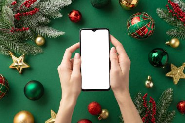 Noel konsepti. Akıllı telefon kırmızı altın sarısı takı yıldız süslemeleri ökse otu üzümleri ve boş alan ile izole edilmiş yeşil arka planda köknar dalları.