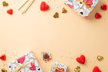 Valentine's Day concept. Top view photo of stylish gift boxes heart shaped candies straws candles and golden confetti on isolated pastel beige background with empty space
