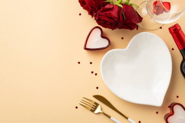 Valentine's Day concept. Top view photo of heart shaped dish candles knife fork wine bottle wineglass bouquet of red roses and confetti on isolated pastel beige background with copyspace