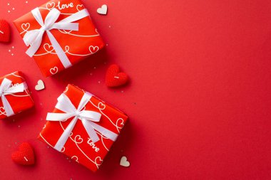 Valentine's Day concept. Top view photo of gift boxes with white ribbon bows heart shaped candles and sequins on isolated red background with copyspace