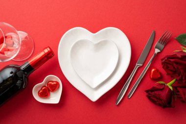 Valentine's Day concept. Top view photo of heart shaped plates cutlery wine bottle glass roses and chocolate candies on isolated red background with copyspace