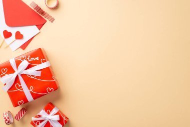 Valentine's Day concept. Top view photo of red gift boxes with ribbon bows envelope with postcard paper hearts and decorative tape on isolated pastel beige background with empty space