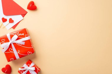 Valentine's Day concept. Top view photo of red gift boxes with ribbon bows envelope with postcard paper hearts and candles on isolated pastel beige background with empty space