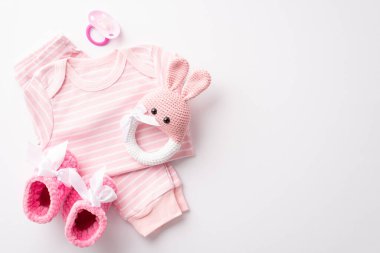 Top overhead above flat lay view photo of baby girl clothes set shirt and pants in light pink color pacifier rattle isolated pink color backdrop with copy space