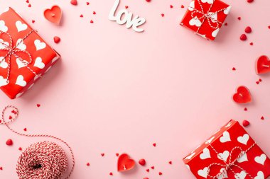Valentine's Day concept. Top view photo of gift boxes heart shaped candles inscription love spool of twine and sprinkles on isolated pastel pink background with copyspace in the middle