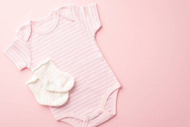 Infant clothes concept. Top view photo of pink bodysuit and tiny socks on isolated pastel pink background