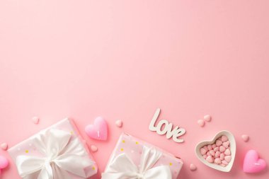Valentine's Day concept. Top view photo of present boxes with white ribbon bows heart shaped saucer with sprinkles candles and inscription love on isolated pastel pink background with empty space