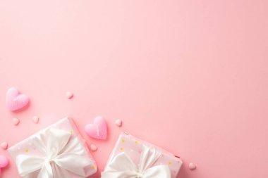Valentine's Day concept. Top view photo of gift boxes with white ribbon bows heart shaped candles and sprinkles on isolated pastel pink background with copyspace