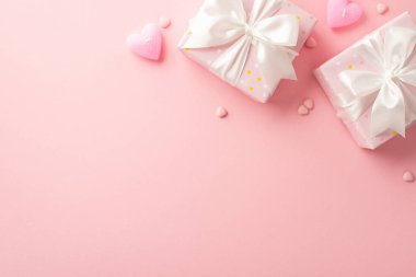 Valentine's Day concept. Top view photo of present boxes with silk ribbon bows heart shaped candles and sprinkles on isolated light pink background with copyspace