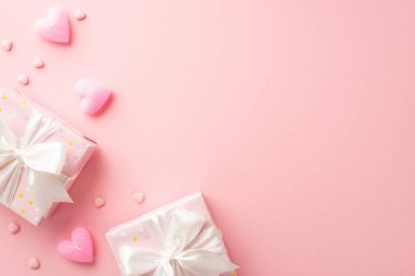 Valentine's Day concept. Top view photo of trendy gift boxes with satin ribbon bows heart shaped candles and sprinkles on isolated pastel pink background with copyspace