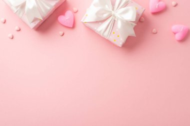 St Valentine's Day concept. Top view photo of big present boxes with satin ribbon bows heart shaped candles and sprinkles on isolated light pink background with blank space