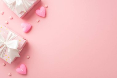 Saint Valentine's Day concept. Top view photo of stylish gift boxes with white ribbon bows heart shaped candles and sprinkles on isolated pastel pink background with blank space