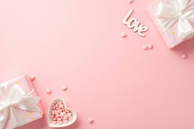 St Valentine's Day concept. Top view photo of present boxes with silk ribbon bows heart shaped saucer with sprinkles and inscription love on isolated pastel pink background with blank space
