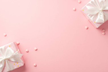 St Valentine's Day concept. Top view photo of stylish present boxes with white ribbon bows and heart shaped sprinkles on isolated pastel pink background with blank space