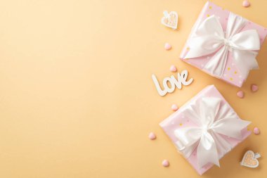 Valentine's Day concept. Top view photo of gift boxes with white ribbon bows heart shaped sprinkles decorative clips and inscription love on isolated pastel beige background with copyspace