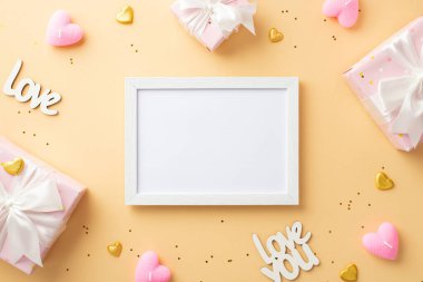 Valentine's Day concept. Top view photo of white photo frame present boxes with ribbon bows inscriptions love candles golden hearts and sequins on isolated pastel beige background with empty space