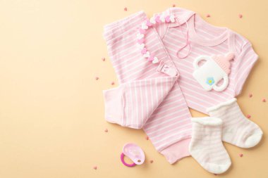 Baby shower concept. Top view photo of infant clothes pink shirt pants socks milk bottle shaped teether dummy chain and sprinkles on isolated pastel yellow background with copyspace