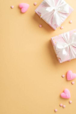 Valentine's Day concept. Top view vertical photo of pink gift boxes with white ribbon bows heart shaped candles and sprinkles on isolated pastel beige background with empty space