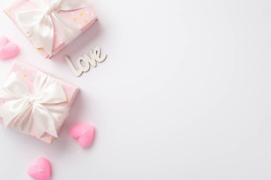 Valentine's Day concept. Top view photo of pastel pink gift boxes with silk ribbon bows heart shaped candles and inscription love on isolated white background with copyspace