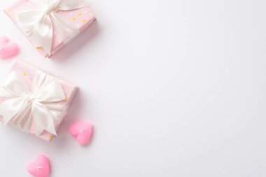 Saint Valentine's Day concept. Top view photo of pastel pink present boxes with silk ribbon bows and heart shaped candles on isolated white background with copyspace