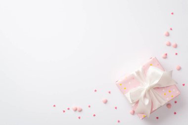 Valentine's Day concept. Top view photo of pastel pink giftbox with silk ribbon bow and heart shaped sprinkles on isolated white background with blank space