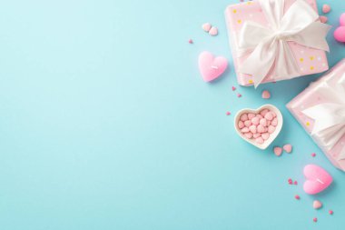 Valentine's Day concept. Top view photo of light pink gift boxes with white ribbon bows candles and heart shaped saucer with sprinkles on isolated pastel blue background with empty space