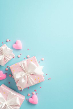 St Valentine's Day concept. Top view vertical photo of pink gift boxes with silk ribbon bows heart shaped candles and sprinkles on isolated light blue background with blank space