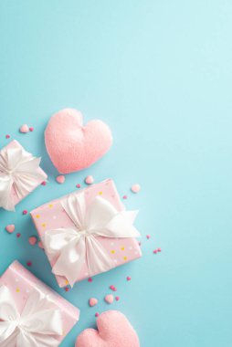 Valentine's Day concept. Top view vertical photo of pink gift boxes with silk ribbon bows heart shaped fluffy toy and sprinkles on isolated pastel blue background with copyspace