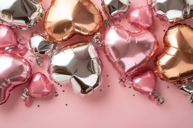 St Valentine's Day concept. Top view photo of heart shaped shiny pink silver golden balloons and confetti on isolated pastel pink background