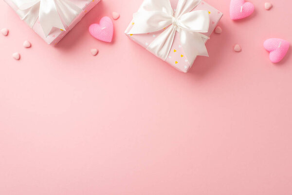 St Valentine's Day concept. Top view photo of big present boxes with satin ribbon bows heart shaped candles and sprinkles on isolated light pink background with blank space