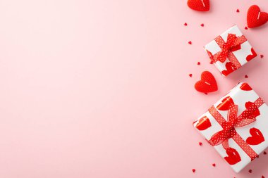 Valentine's Day concept. Top view photo of gift boxes ribbon heart shaped candles and sprinkles on isolated light pink background with empty space