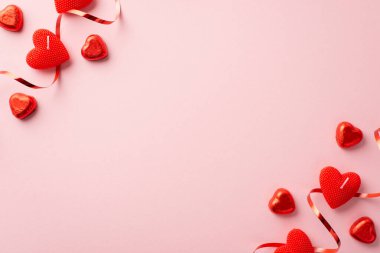 St Valentine's Day concept. Top view photo of red heart shaped candles chocolate candies serpentine and confetti on isolated pastel pink background with copyspace