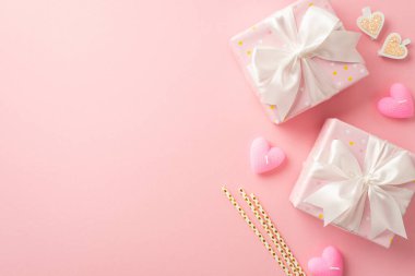 Valentine's Day concept. Top view photo of stylish gift boxes with white ribbon bows straws decorative clips and heart shaped candles on isolated pastel pink background with blank space