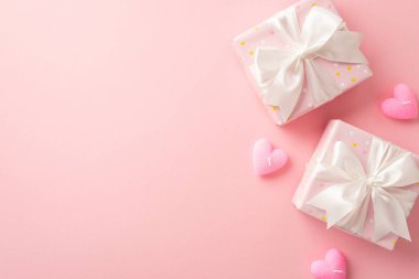 Valentine's Day concept. Top view photo of stylish gift boxes with white ribbon bows and heart shaped candles on isolated light pink background with copyspace