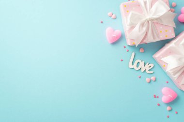 Valentine's Day concept. Top view photo of light pink gift boxes with white ribbon bows inscription love heart shaped candles and sprinkles on isolated pastel blue background with empty space