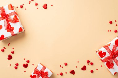 Valentine's Day concept. Top view photo of white present boxes with ribbon bows red hearts and sprinkles on isolated pastel beige background with empty space