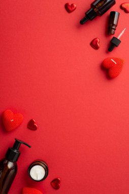 Skincare concept. Top view vertical photo of amber glass cosmetic bottles heart shaped candles and confetti on isolated red background with copyspace