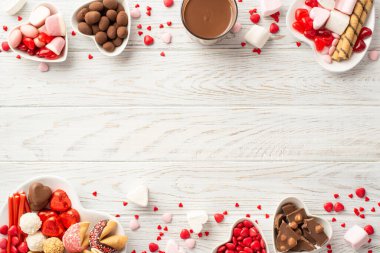 Valentine's Day concept. Top view photo of heart shaped plates with sweets chocolate candies cookies and glass of beverage on white wooden table background