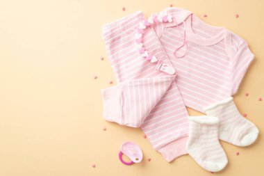 Baby accessories concept. Top view photo of infant clothes pink shirt pants socks pacifier teether chain and sprinkles on isolated pastel yellow background with copyspace