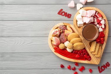 Sevgililer Günü konsepti. Tahta kalp şeklindeki servis tepsisinin en üstteki fotoğrafı şekerli servis tepsisi. Bir bardak sıcak çikolata ve yazıtlar. Gri ahşap masa zemininde, kopyalanmış aşk.