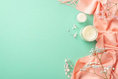 Hello spring concept. Top view photo of candles in glass holders blue and pink gypsophila flowers and soft scarf on isolated turquoise background with blank space