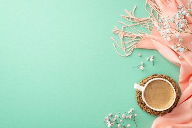 Hello spring concept. Top view photo of mug of frothy coffee on wicker serving mat gypsophila flowers and pink cozy plaid on isolated teal background with copyspace