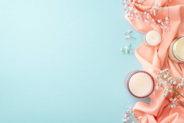 Spring mood concept. Top view photo of candles in glasses gypsophila flowers and pink soft plaid on isolated pastel blue background with blank space