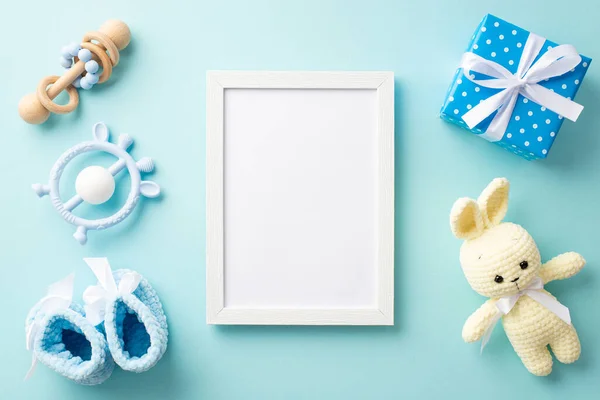 stock image Baby concept. Top view photo of photo frame blue knitted booties present box with bow bunny toy teether and wooden rattle on isolated pastel blue background with copyspace