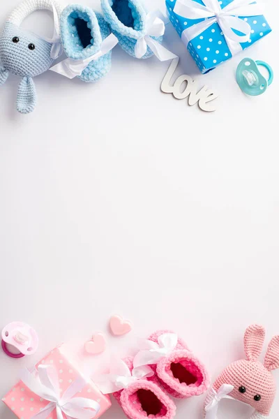 Gender reveal party concept. Top view vertical photo of pink and blue knitted booties gift boxes bunny rattle toys inscription love hearts and soothers on isolated white background with copyspace